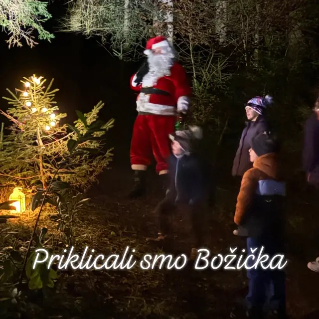 Božiček z otroki v večernem gozdu ob okrašeni smrečici