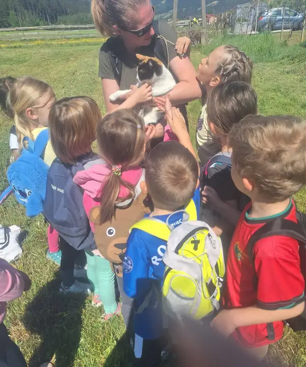 Otroci se zberejo okoli vzgojiteljice, ki v naročju drži žival